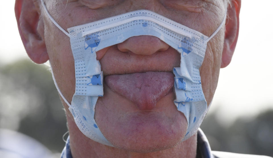 A participant in a demonstration protests on the Rhine meadows with a cut-up mask and tongue stuck out against the measures to combat the coronavirus in Duesseldorf, Germany, Sunday, Sept.20, 2020. (Roberto Pfeil/dpa via AP)