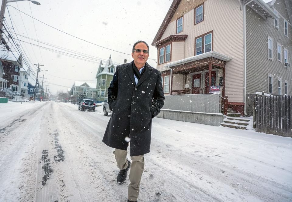 Former Providence Mayor Angel Taveras walks by two of the triple-deckers he lived in while growing up on Potters Avenue in Providence.