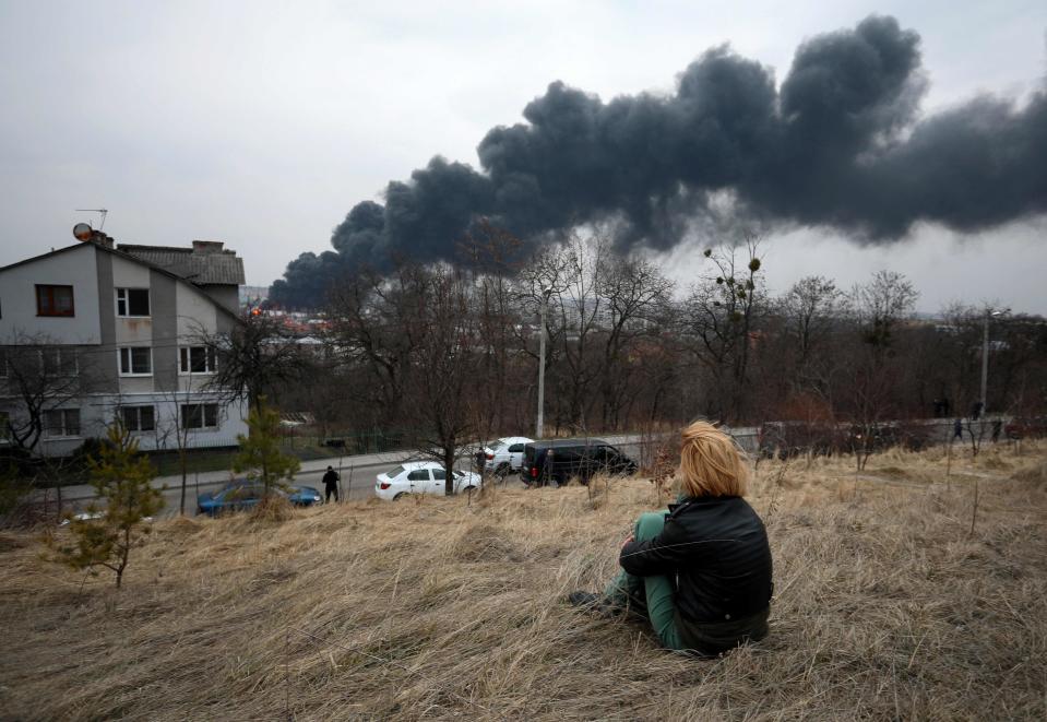 A youth sits on the top of a hill watching dark smoke and flames rising from a fire after a missile strike in Lviv (AFP/Getty)