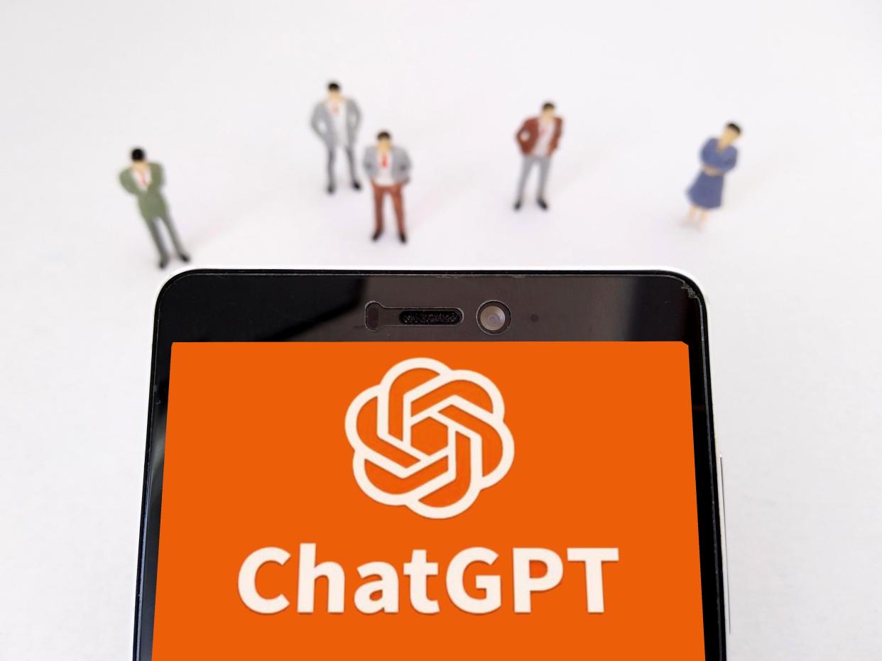 A group of people standing around a phone with a large OpenAI and ChatGPT logos.