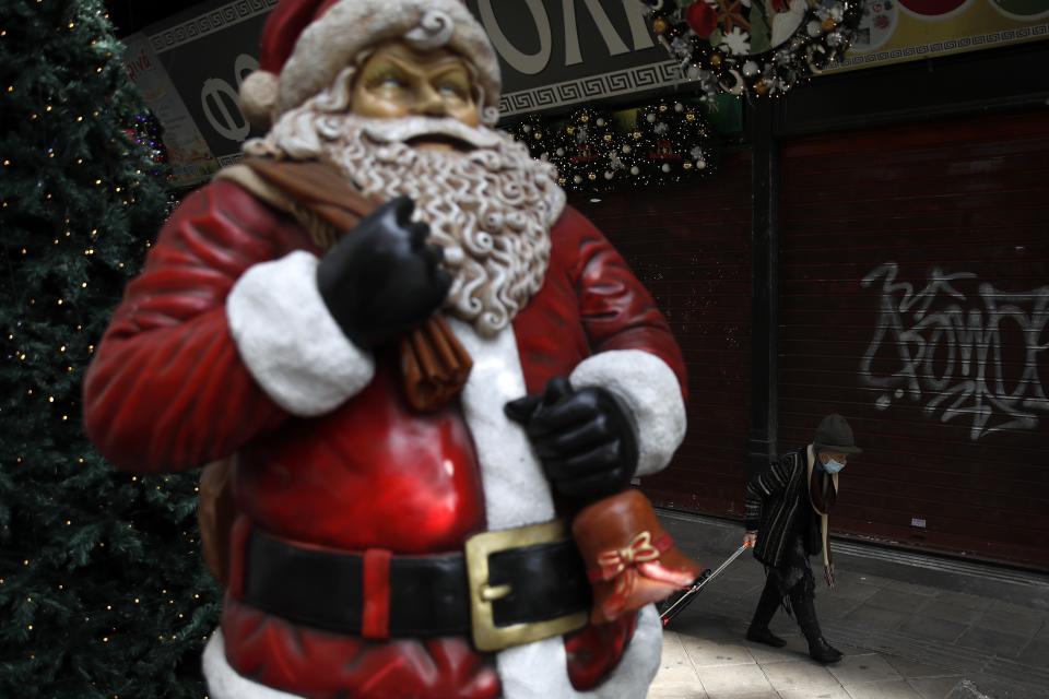 A woman wearing a face mask against the spread of coronavirus, passes a Santa Claus outside a store in Athens, Tuesday, Nov. 24, 2020. Greece is set to extend its lockdown measures beyond the end of November given the spread of COVID-19 and the pressure on hospitals, the country's health minister warned Monday. (AP Photo/Thanassis Stavrakis)