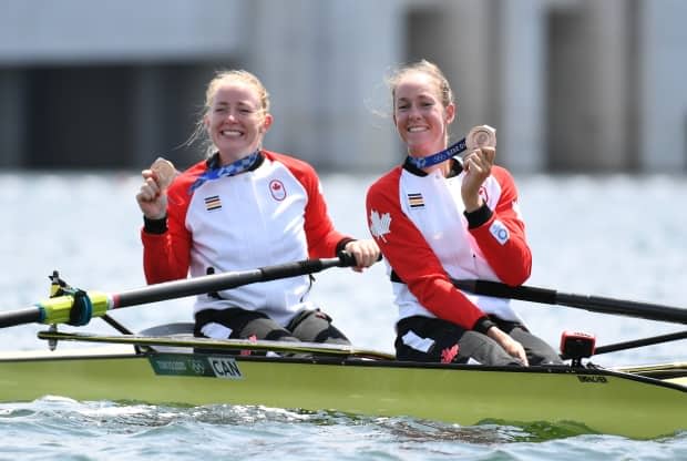 Canadian rowers Caileigh Filmer, left, and Hillary Janssens hold up their bronze medals after reaching the podium in the women's pair final on Thursday at the Tokyo Olympics. (Piroschka Van De Wouw/Reuters - image credit)