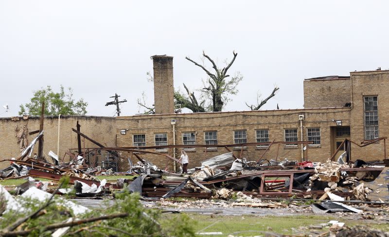 A woman walks through the debris scattered around the damaged Van Intermediate School after a tornado swept through the area the previous night in Van, Texas