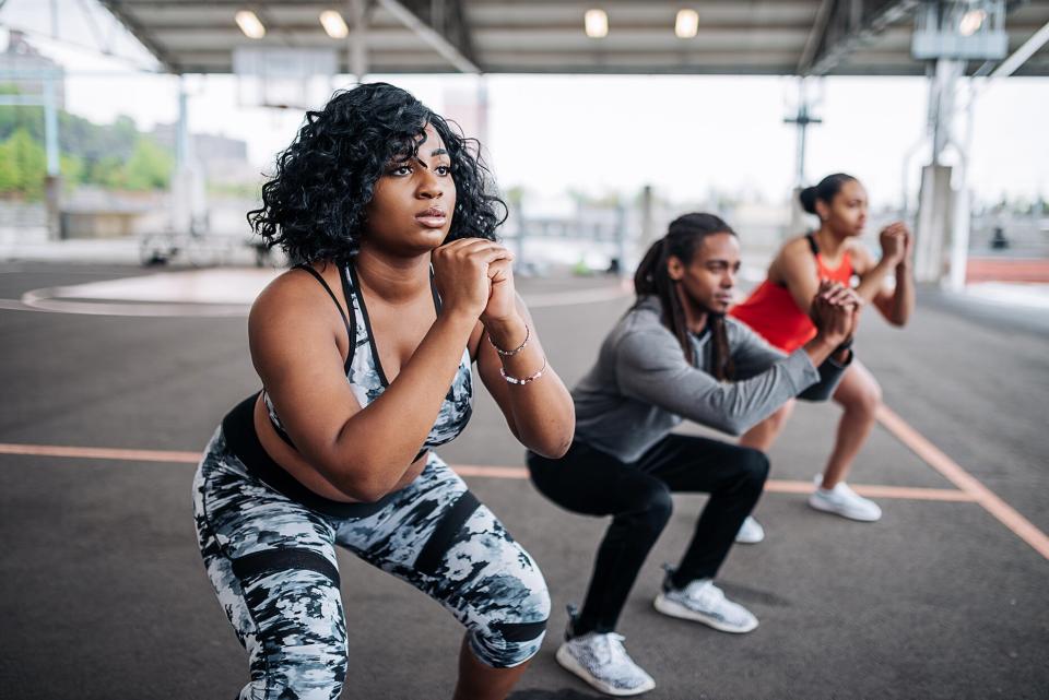 three people in workout gear doing squat holds on a basketball court