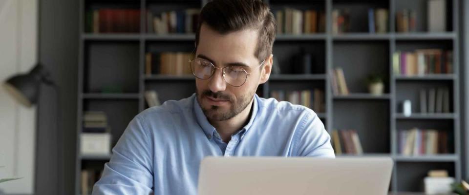 Confident businessman wearing glasses writing notes or financial report, sitting at desk with laptop, focused serious man working with paper documents, student studying online, research work