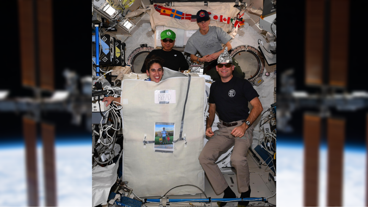  An image of four astronauts in costumes at the front. the background shows a blurry image of the international space station. 