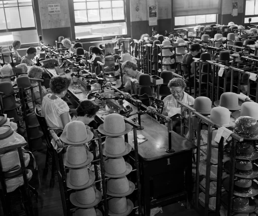 1960s HAT MAKING FACTORY WITH ROWS OF WOMEN AT LONG TABLE HAND TRIMMING STETSON HATS