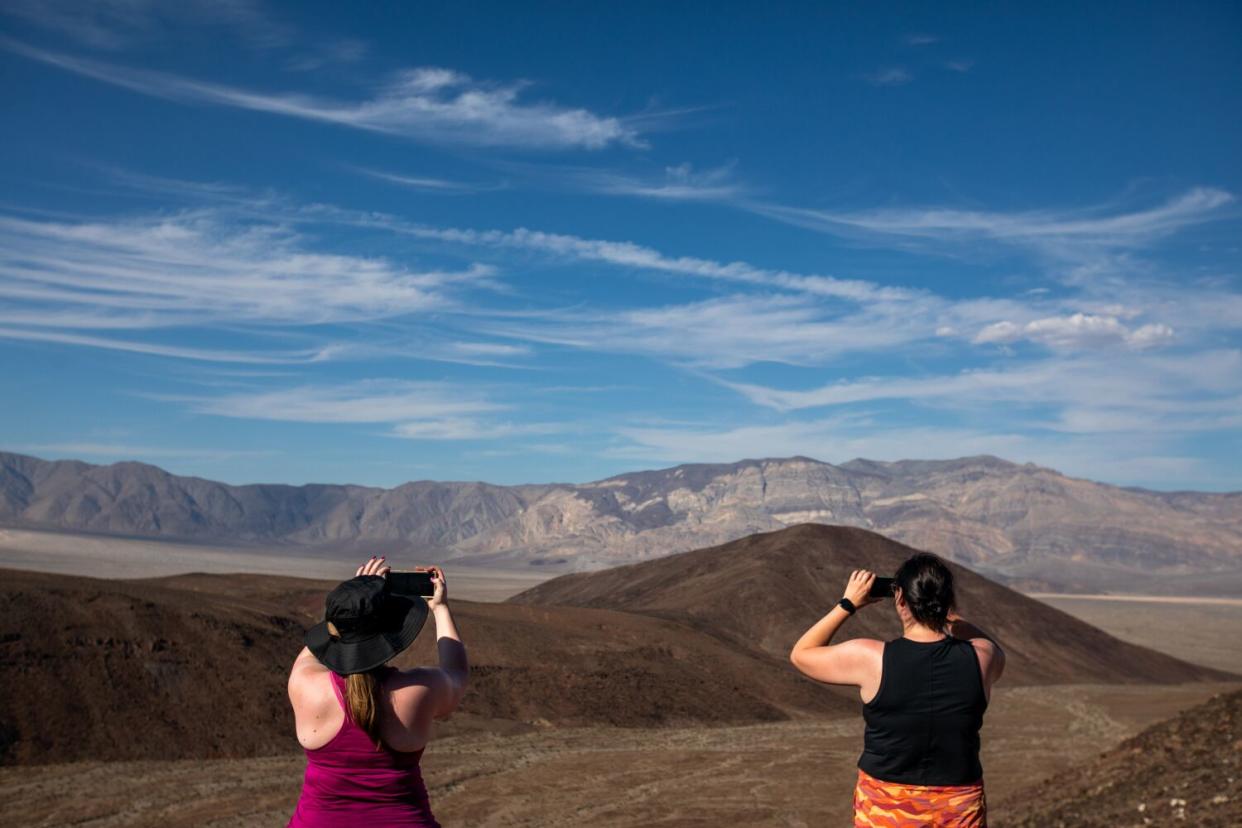 Two people photograph mountains on the horizon.