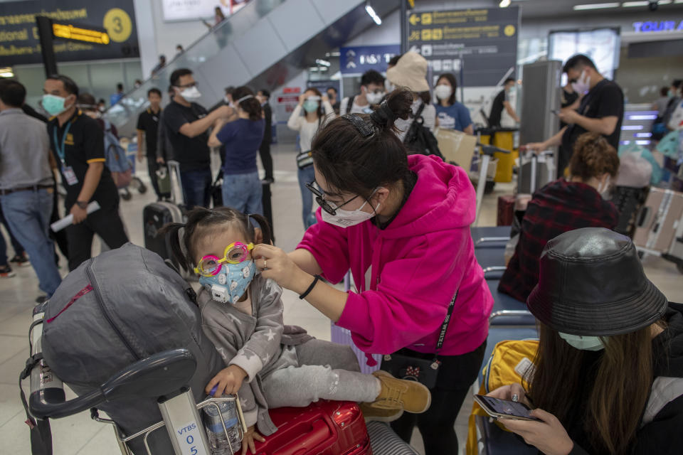 A tourist from Wuhan, China, adjusts the face mask of a child as they stand in a line for a charter flight back to Wuhan at the Suvarnabhumi airport, Bangkok, Thailand, Friday, Jan. 31, 2020. A group of Chinese tourists who have been trapped in Thailand since Wuhan was locked down due to an outbreak of new virus returned to China on Friday. (AP Photo/Gemunu Amarasinghe)