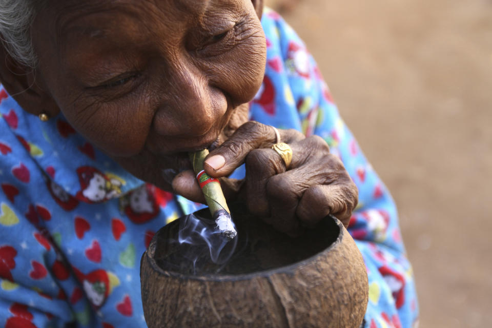 In this photo taken on Feb. 6, 2012, a woman smokes a cheroot in front of a temple in Bagan, Myanmar. As the country sheds its past as an isolated military dictatorship and taboo travel destination it is becoming a new global hotspot - topping tourism lists as the must-see place to visit in 2012. Recent reforms have encouraged more tourists to visit the country. (AP Photo/Pailin Wedel)