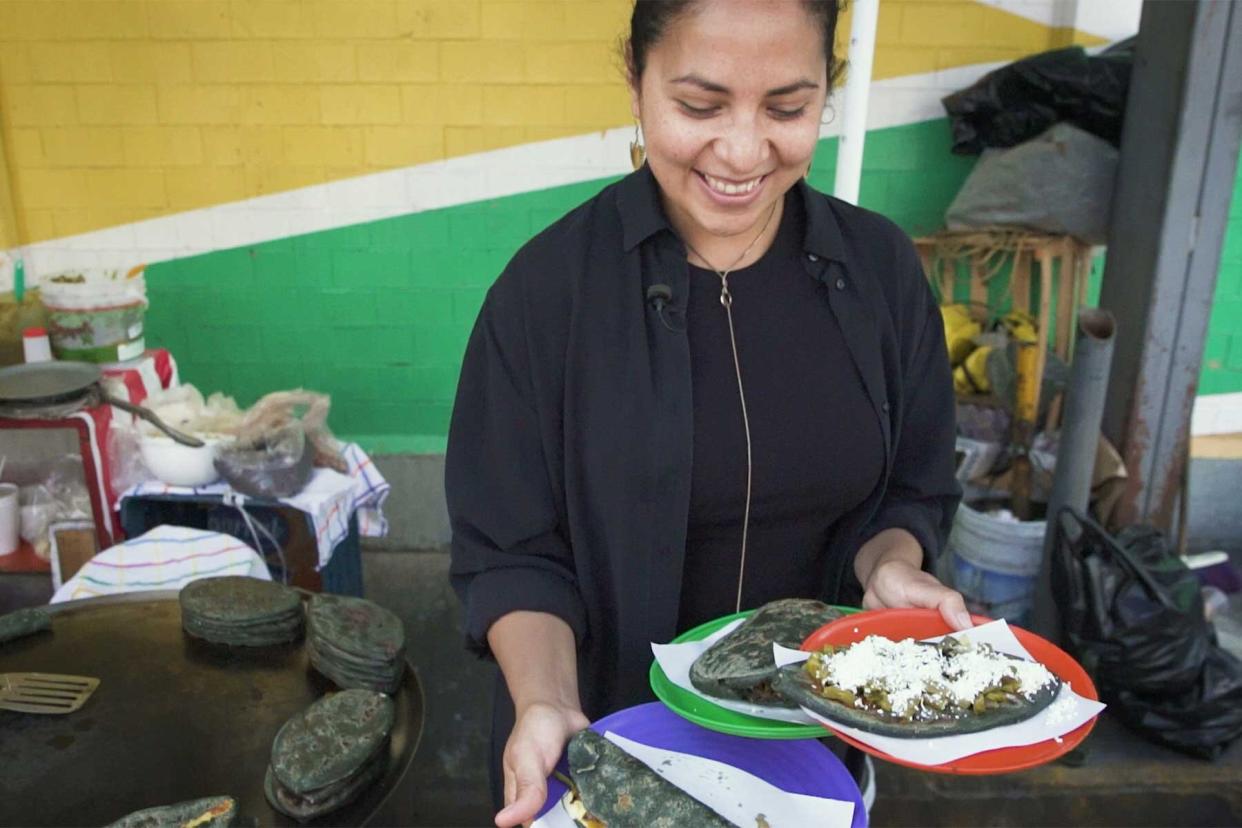 Anais Martinez holding plates of Mexican street food on her episode of Walk With T+L