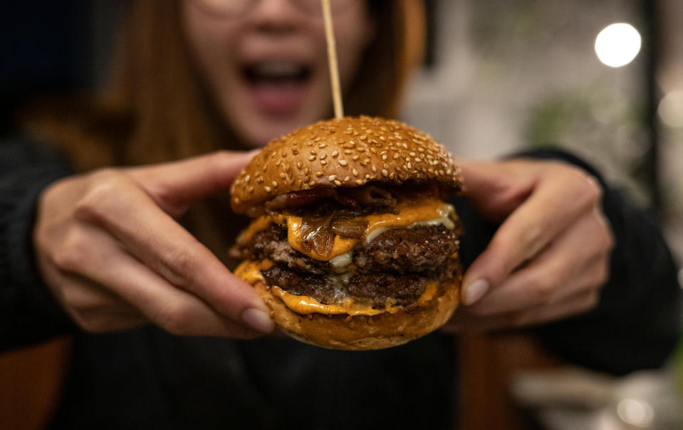 Closeup of a woman's hands holding a giant burger with multiple patties
