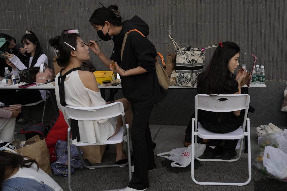 Models put on make up while others take a lunch break during Auto China 2024 in Beijing, Thursday, April 25, 2024. Global automakers and EV startups unveiled new models and concept cars at China's largest auto show on Thursday, with a focus on the nation's transformation into a major market and production base for digitally connected, new-energy vehicles. (AP Photo/Ng Han Guan)