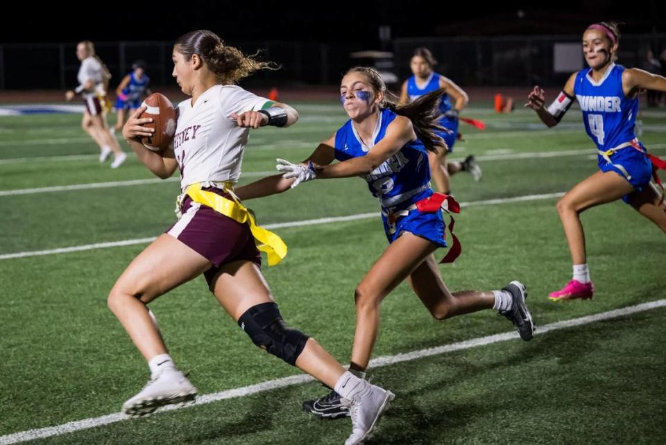 Rocklin Thunder defender Caroline Wuelfing (2), center, pulls the flag off Whitney Wildcats quarterback Alex Maday (11) on a keeper during the second half at the high school girls flag football game Thursday, Sept. 28, 2023, at Rocklin High School. During the inaugural “Battle for the Belt” showdown, the school took aim at its previous record for attendance at a girls sporting event.