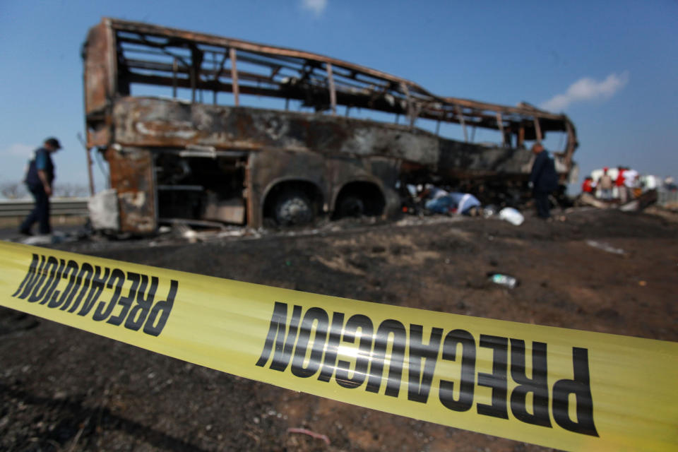 In this Sunday, April 13, 2014 photo, caution tape creates a perimeter around a passenger bus that burst into flames after slamming into a broken-down truck near the town of Ciudad Isla in the Gulf state of Veracruz, Mexico. Dozens of people traveling on the bus to Mexico City burned to death inside the bus. Both state and federal officials said that only a few people survived the crash. (AP Photo/Felix Marquez)
