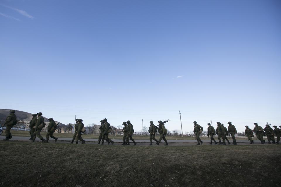 Military personnel, believed to be Russian servicemen, walk outside the territory of a Ukrainian military unit in the village of Perevalnoye outside Simferopol