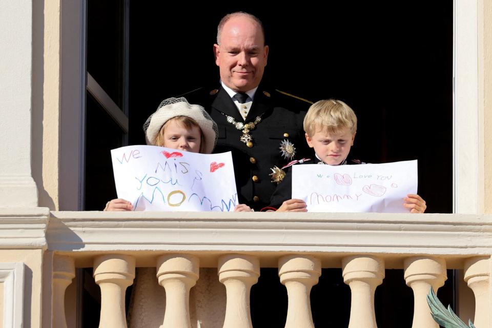 Prince Albert II of Monaco, Princess Gabriella and Prince Jacques stand with a message for Princess Charlene at the balcony of Monaco Palace