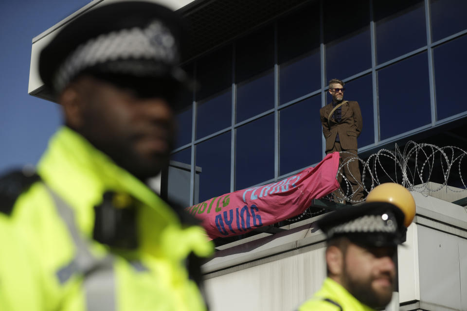 Police Officers stand guard as an Extinction Rebellion demonstrator ties a banner to a raised area at City Airport in London, Thursday, Oct. 10, 2019. Some hundreds of climate change activists are in London during a fourth day of world protests by the Extinction Rebellion movement to demand more urgent actions to counter global warming. (AP Photo/Matt Dunham)