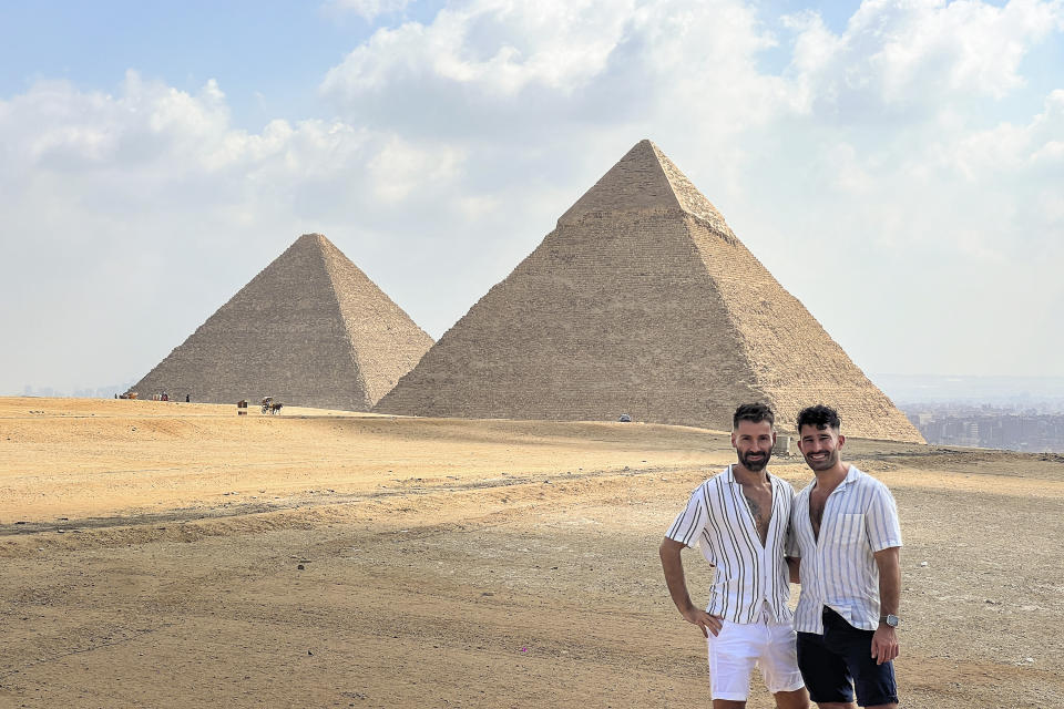 This 2023 photo shows Stefan Arestis, right, and Sebastien Chaneac, at the Pyramids in Egypt. The two are globetrotters who run the LGBTQ+-focused travel blog The Nomadic Boys. They published a travel guide this year, “Out in the World: The Gay Guide to Travelling with Pride.” (The Nomadic Boys via AP)