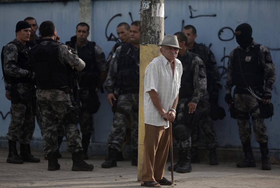 An elderly man stands next to police officers as they patrol at the Vila Kennedy slum during an operation to install the Police Peacekeeping Unit (UPP) in the region in Rio de Janeiro March 13, 2014. The introduction of the peacekeeping program in the region is part of efforts to crack down on crime and increase security as the city prepares to host the 2014 World Cup soccer tournament and the 2016 Olympic Games. REUTERS/Ricardo Moraes (BRAZIL - Tags: CRIME LAW CIVIL UNREST)