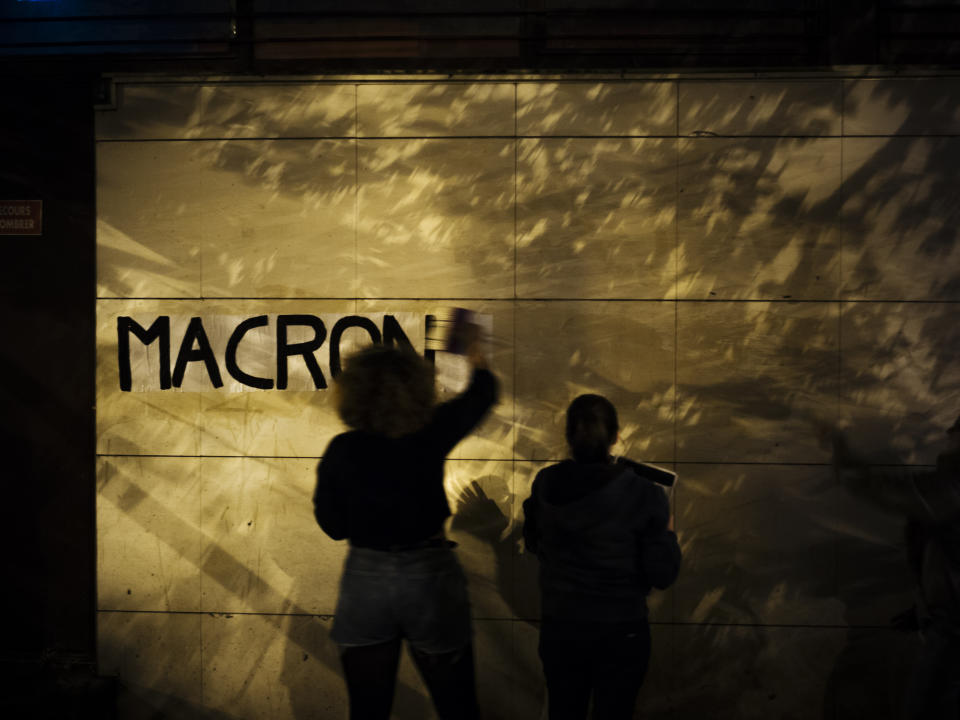 In this Oct. 24 2019, photo, Maya, 19, a student from Versailles pastes a slogan with the name of French President Emmanuel Macron in the evening in the south of Paris. France, a country that has prided itself on gender equality, is beginning to pay serious attention to its yet-intractable problem of domestic violence. Under cover of night, activists have glued slogans to the walls to draw attention to domestic violence, a problem French President Emmanuel Macron has called "France's shame." (AP Photo/Kamil Zihnioglu)