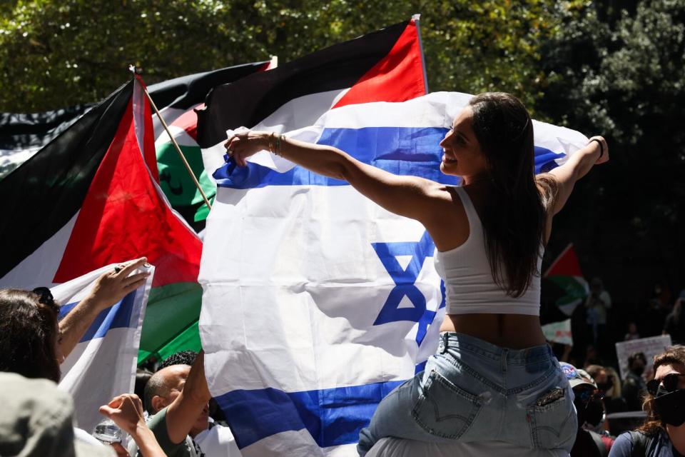 A protestor in support of Israel waves an Israeli flag while surrounded by pro-Palestinian