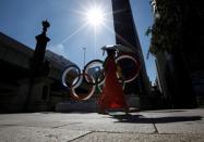 A woman holding a sunshade walks past Olympic rings displayed at Nihonbashi district in Tokyo