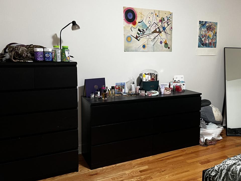Bedroom of apartment with view of full-length mirror and two black dressers with items on top.