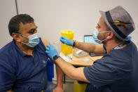 A man receives a dose of the Pfizer COVID-19 vaccine at Swaminarayan School vaccination centre, in London, Saturday, Dec. 4, 2021. Britain says it will offer all adults a booster dose of vaccine within two months to bolster the nation's immunity as the new omicron variant of the coronavirus spreads. New measures to combat variant came into force in England on Tuesday, with face coverings again compulsory in shops and on public transport. (AP Photo/Alberto Pezzali)