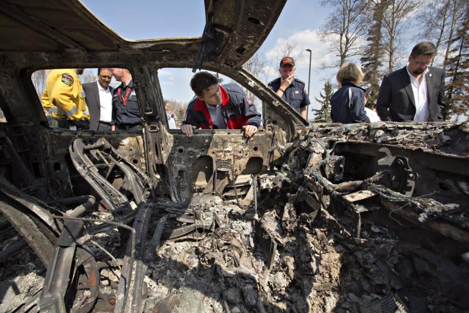 Prime Minister Justin Trudeau, centre left, and Fort McMurray Fire Chief Darby Allen, centre right, look over a burnt out car during a visit to Fort McMurray, Alta., on Friday, May 13, 2016. THE CANADIAN PRESS/Jason Franson