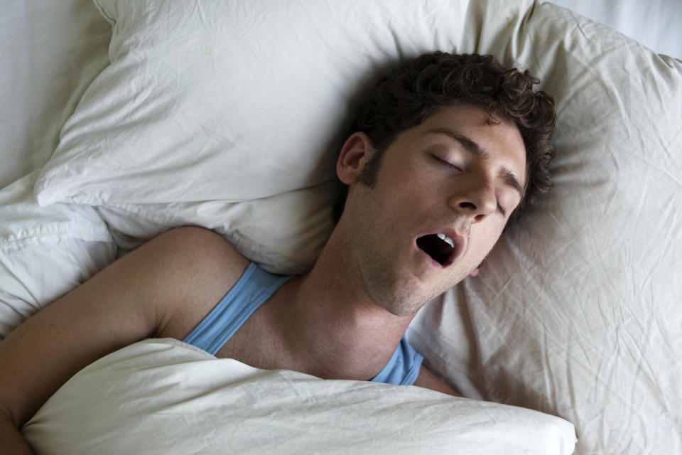 A person sleeps in bed with their mouth open