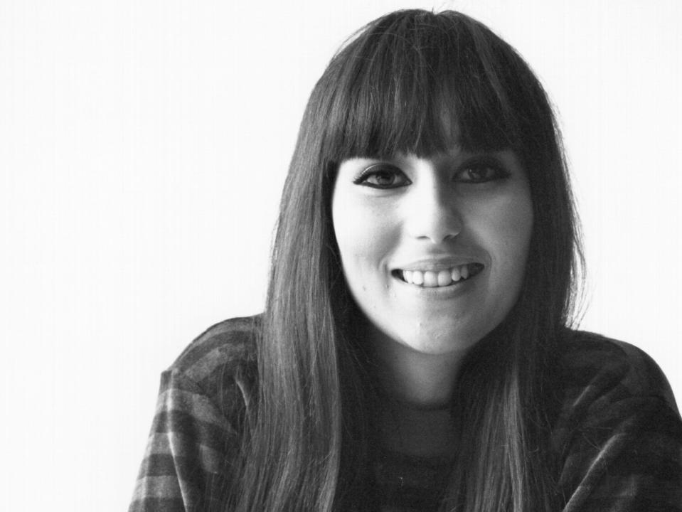 A black and white photo of Cher with bangs and a striped sweater on.