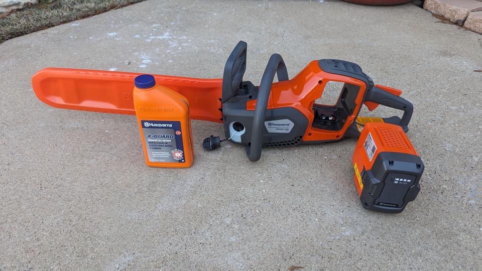 Image showing the Husqvarna Power Axe 350i Cordless Electric Chainsaw, a bottle of chain oil and the battery, not yet inserted
