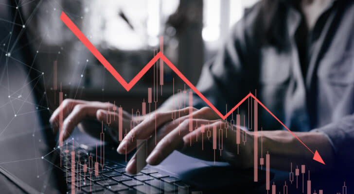 Grayish photo of investor's hands hovering over laptop with red stock graph showing downward arrow overlayed on top of the image. falling stocks