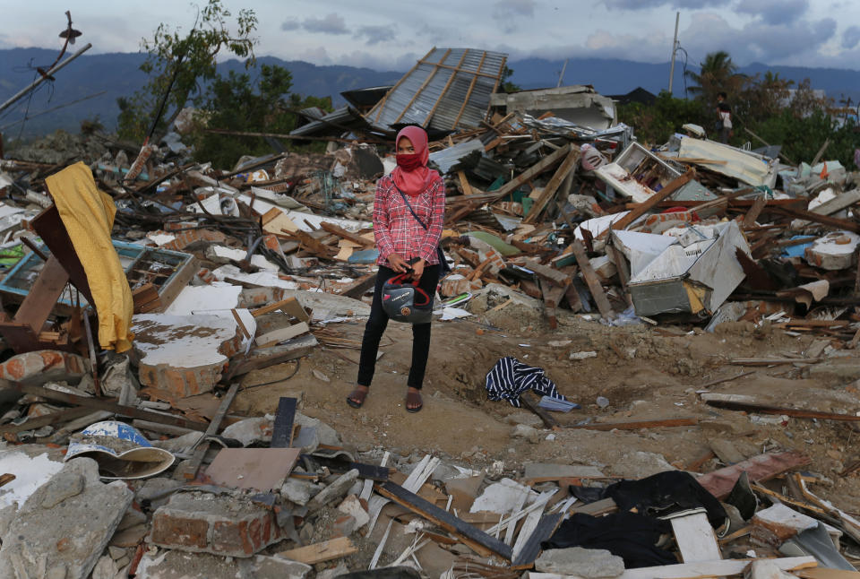 A woman stands on the rubble of houses at Petobo neighborhood which was wiped out by earthquake-triggered liquefaction in Palu, Central Sulawesi, Indonesia, Sunday, Oct. 7, 2018. Indonesia's disaster agency said the number of dead had climbed and many more people could be buried, especially in the Palu neighborhoods of Petobo and Balaroa, where thousands of homes were damaged or sucked into deep mud when the Sept. 28 quake caused loose soil to liquefy. (AP Photo/Dita Alangkara)