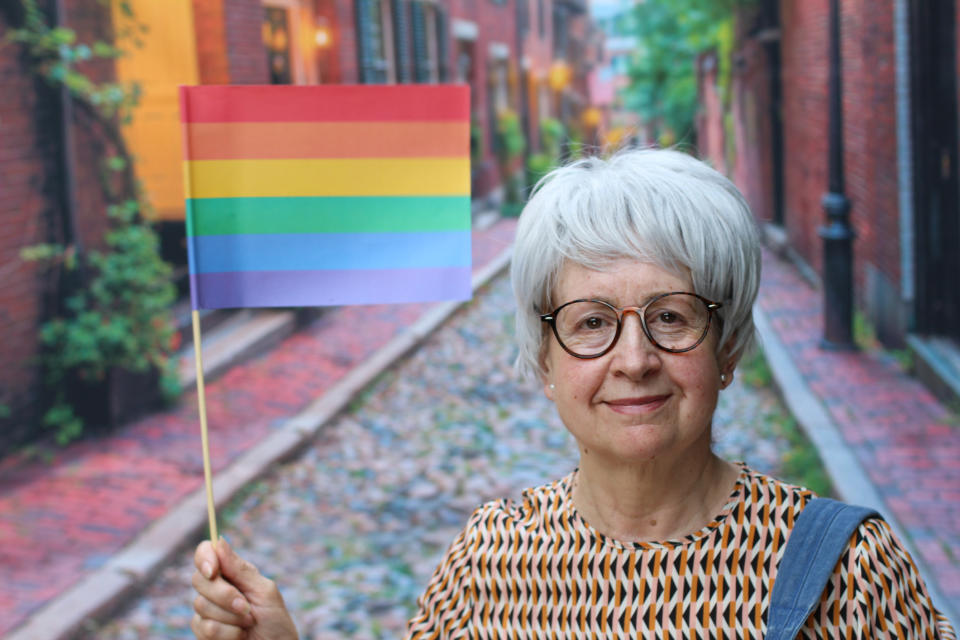 An older person holding the LGBTQ+ flag as the stand in the street