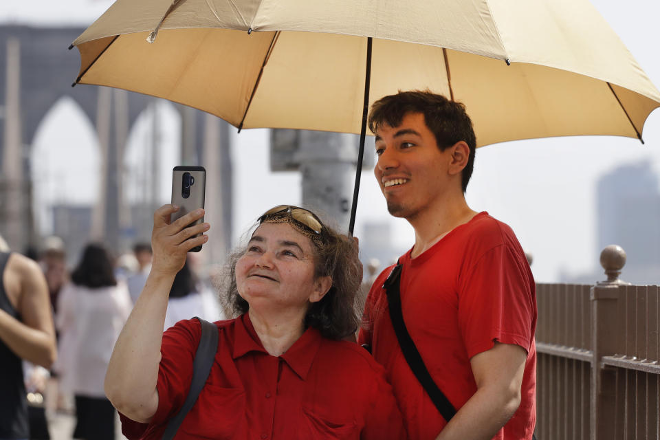 Luz Palomino and her son Roger take a photo while shading themselves under an umbrella on the Brooklyn Bridge, Wednesday, Aug. 29, 2018 in New York. The National Weather Service says temperatures in the 90s combined with high humidity are pushing the heat index past 100. (AP Photo/Mark Lennihan)