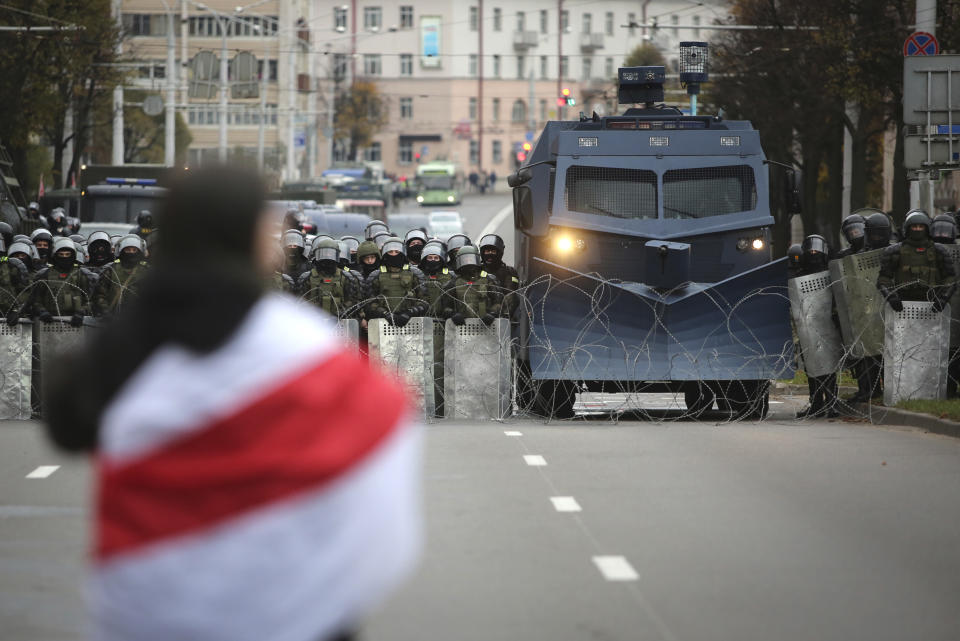 A protester draped in an old Belarusian national flag stands in front of a police line during an opposition rally to protest the official presidential election results in Minsk, Belarus, Sunday, Oct. 25, 2020. The demonstrations were triggered by official results giving President Alexander Lukashenko 80% of the vote in the Aug. 9 election that the opposition insists was rigged. Lukashenko, who has ruled Belarus with an iron fist since 1994, has accused the United States and its allies of fomenting unrest in the ex-Soviet country. (AP Photo)