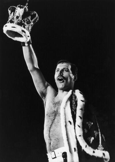 Freddie Mercury holding crown up to the sky, with royal cloak draped on other side of body
