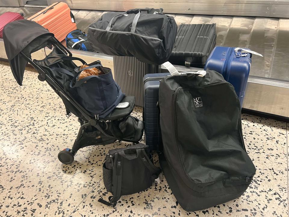 Several large pieces of luggage, a stroller, and smaller bags sit next to a baggage claim carousel at an airport.