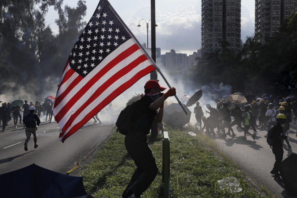 FILE - In this Aug. 5, 2019, file photo, a protester runs with a United States flag as tear gas are released on protesters in Hong Kong. China’s central government has dismissed Hong Kong pro-democracy protesters as clowns and criminals while bemoaning growing violence surrounding the monthslong demonstrations. (AP Photo/Kin Cheung, File)