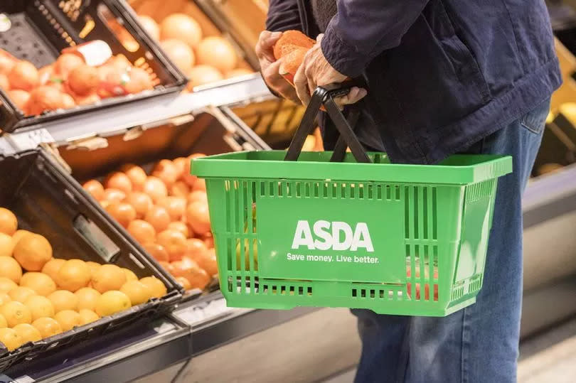 A customer holds a basket of groceries inside an Asda store.