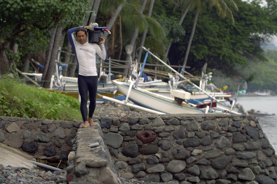 Made Partiana walks along beach area at Les, Bali, Indonesia, on April 11, 2021, as he prepares to catch aquarium fish. Over the years Partiana began to notice the reef was changing. “I saw the reef dying, turning black,” he says. “You could see there were less fish.” (AP Photo/Alex Lindbloom)