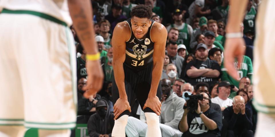 Giannis Antetokounmpo grins while he rests his hands on his knees during a game.