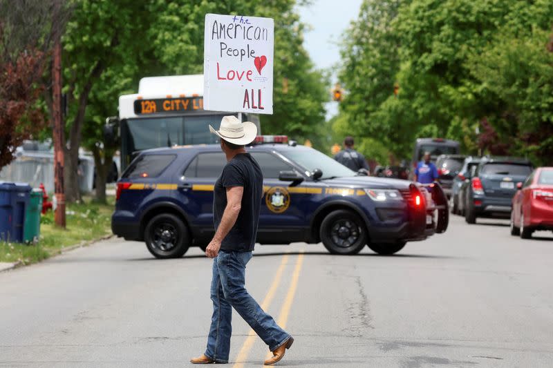 A man walks with a sign near the scene of a weekend shooting at a Tops supermarket in Buffalo, New York
