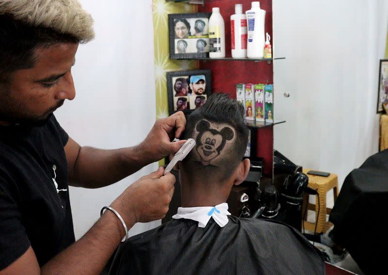 Rajwinder Singh Sidhu shaves the hair of a customer in the shape of Mickey Mouse inside his shop in Dabwali