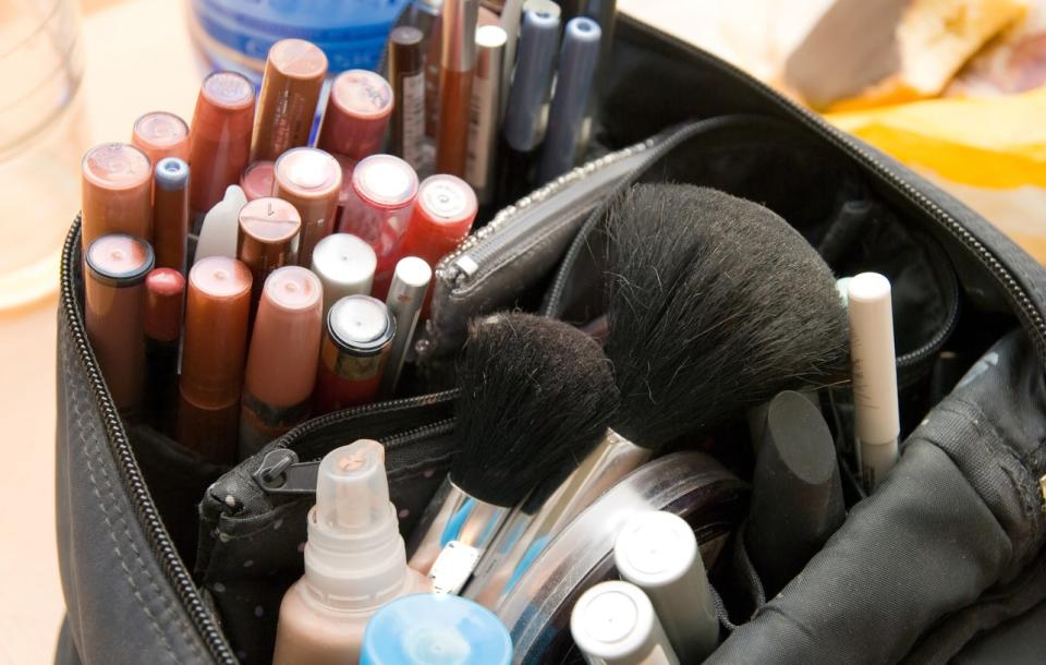 Cometic brushes, lip glosses, eye pencils and other makeup neatly arranged in a makeup bag.