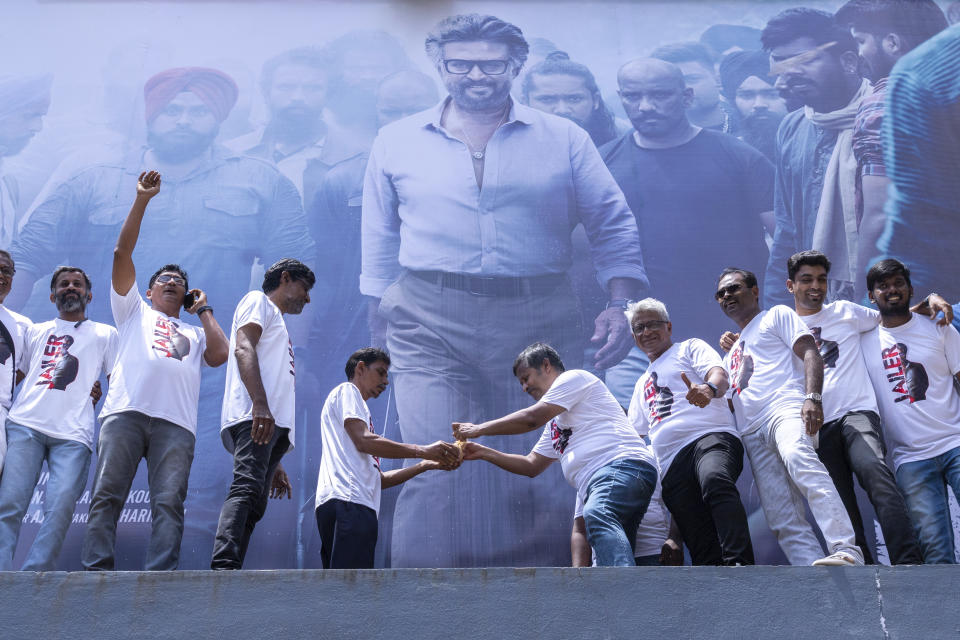 Indian fans prepare to break a coconut before a huge poster of their superstar Rajinikanth, outside a cinema hall as they celebrate the screening of his latest film "Jailer" in Chennai, India, Thursday, Aug. 10, 2023. (AP Photo/ R. Parthibhan)