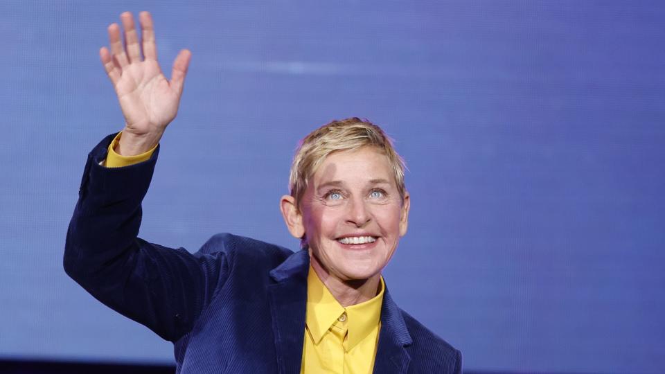 ellen degeneres waving to an audience with her right hand while taking the stage for a panel