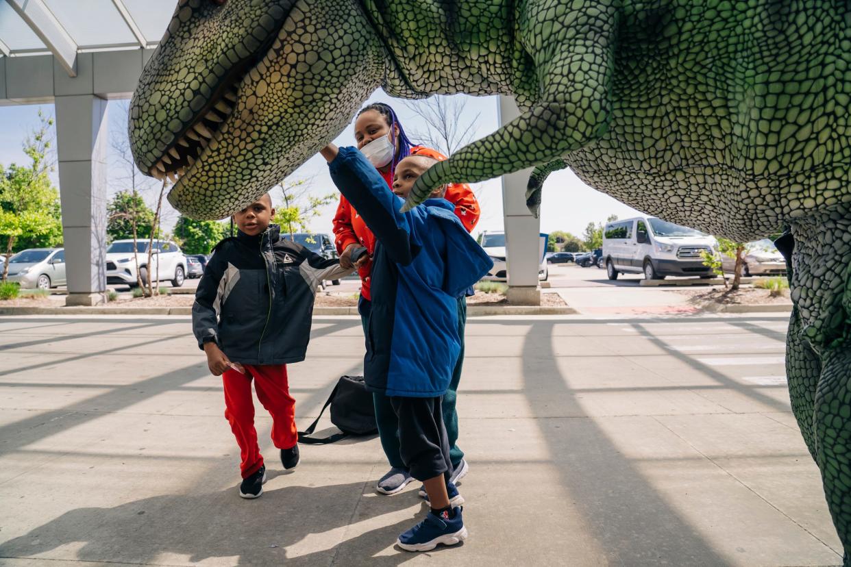 Tabitha Bowles, of Detroit, holds her sons as they touch an animatronic dinosaur outside of the Detroit Medical Center Children's Hospital of Michigan Specialty Center from the national touring Dino & Dragon Stroll event that will take place at Canterbury Village in Lake Orion as the dinosaurs visited children at the DMC Children's Hospital and Specialty Center in Detroit on May 24, 2022.